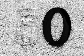 Address number Fifty on rough wall of a house with a peeling Five and a black Zero