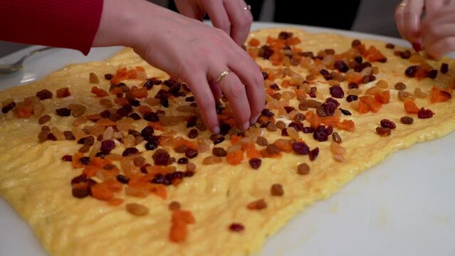 Unrecognizable persons sprinkles raisins on a rolled dough smeared with butter. Prepares cruffin with raisins.