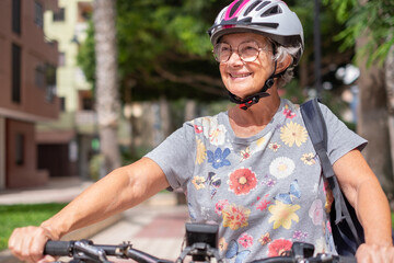 Portrait of happy senior cyclist woman wearing helmet running with electric bicycle in city public park enjoying freedom.  Concept of healthy lifestyle and sustainable mobility