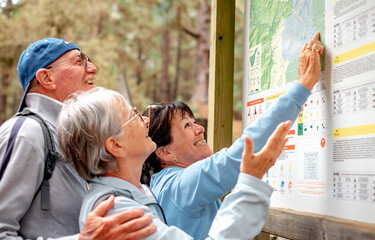 Group of cheerful senior friends in mountain excursion looking the right direction on the map enjoying healthy lifestyle in nature