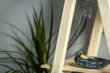 magic smoke from a burning palo santo stick lying on a natural shell incense stand on a wooden shelf in the interior Concept of mental health