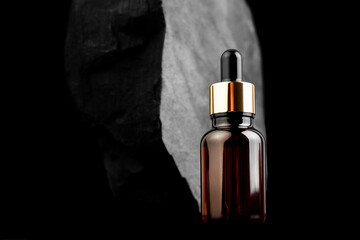 Brown bottle with dropper with a beauty serum granite stone on black background. Glass packaging...