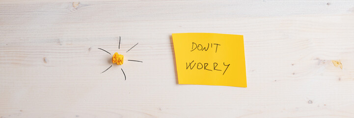 Wide view image of a yellow paper with Dont worry sign on it placed on wooden background