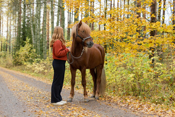 Young female equestrian posing with Icelandic horse in in autumn scenery
