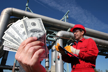 Natural Gas Price as a Concept. Hand holding US dollar bills in front of petroleum engineer inside...