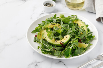 Green vegetable salad with avocado and mix lettuce, arugula on white plate and marble background.