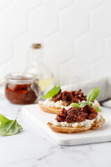 Toast with dried tomatoes in oil, cottage cheese, ricotta cheese, and basil. Bruschetta, snack, appetizers. Sandwiches on white board.