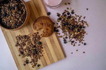 Tuinposter Top view of a bowl of homemade nut and choco granola with a chocolate cookie on a wooden board © Oksana Taran/Wirestock Creators