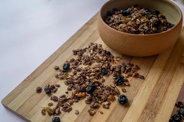 Foto op Canvas Closeup of a bowl of homemade nut and choco granola on a wooden cutting board on a table © Oksana Taran/Wirestock Creators