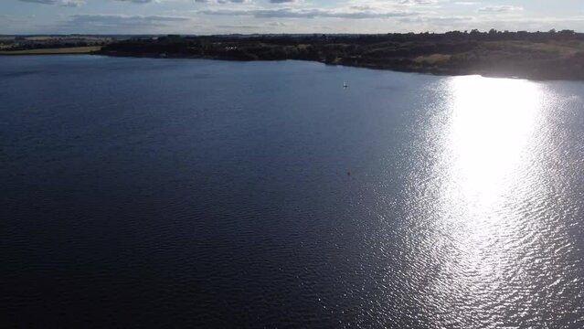 Aerial view of the Pitsford Reservoir with sun reflection and a sailing boat in Northamptonshire, UK