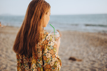 Back view of young girl drinking fresh juice and looking at sunset beach