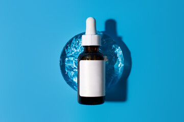 Brown bottle serum dropper pipette with serum on circle, glass podium. Blue background with daylight and the appearance of the texture of the gel. Beauty concept skincare for face and body care.
