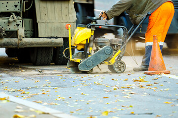 A worker saws asphalt on the road for repair with a special device