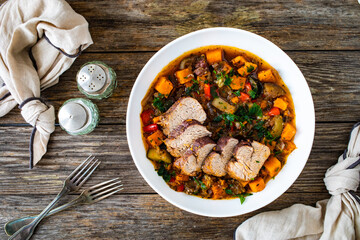 Roast pork loin with sweet potatoes and mix of cooked vegetables served on wooden table

