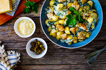Roasted chicken nuggets, spinach, parmesan and noodles served on wooden table