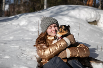 A young girl in the forest in winter holds a dog in her arms and enjoys the weather and the sun outdoors