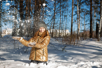 A girl in the winter in the forest rejoices in the snow and throws it up enjoying a weekend in nature in the cold