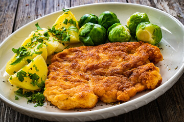 Breaded fried pork chop with boiled potatoes and brussels sprouts  on wooden table
