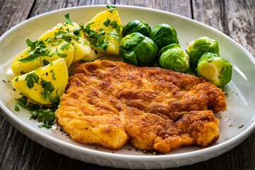 Breaded fried pork chop with boiled potatoes and brussels sprouts  on wooden table
