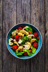 Fresh vegetable salad with cheese - camembert, artichoke, lettuce, cherry tomatoes, cucumber,  pekan nuts, arugula and  spinach  on wooden table
