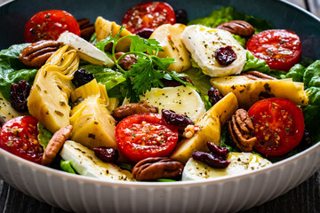 Fresh vegetable salad with cheese - camembert, artichoke, lettuce, cherry tomatoes, cucumber,  pekan nuts, arugula and  spinach  on wooden table
