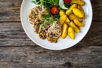 Fried pork loin with baked potatoes and fresh green  vegetables on wooden table
