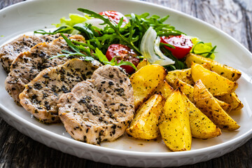 Fried pork loin with baked potatoes and fresh green  vegetables on wooden table
