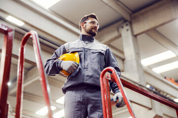 Low angle view of an industry worker standing with a helmet in his hands and monitors works in the...