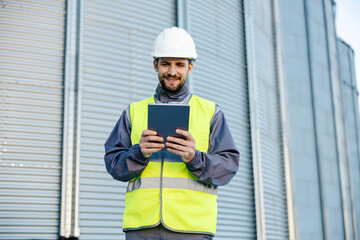 An oil refinery worker stands outside in front of the silos and smiles at the tablet in his hands. © Dusan Petkovic
