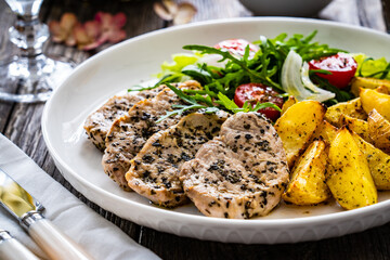 Fried pork loin with baked potatoes and fresh green  vegetables on wooden table

