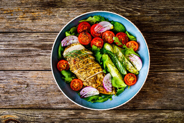 Tasty salad - fried chicken breast, mini tomatoes, cucumber  and fresh green vegetables on wooden background
