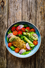 Tasty salad - fried chicken breast, mini tomatoes, cucumber  and fresh green vegetables on wooden background
