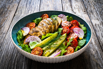 Tasty salad - fried chicken breast, mini tomatoes, cucumber  and fresh green vegetables on wooden background
