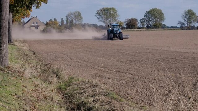 Traktor f&auml;hrt &uuml;ber ein trockenes und abgeerntetes Feld und wirbelt Staubwolken auf