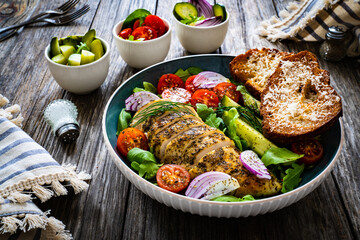 Tasty salad - fried chicken breast, mini tomatoes, cucumber  and fresh green vegetables on wooden background
