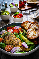 Tasty salad - fried chicken breast, mini tomatoes, cucumber  and fresh green vegetables on wooden background
