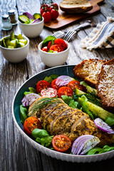 Tasty salad - fried chicken breast, mini tomatoes, cucumber  and fresh green vegetables on wooden background
