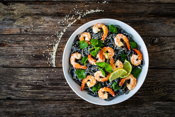 Black rice noodles with fried prawns and coriander on wooden table
