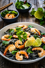 Black rice noodles with fried prawns and coriander on wooden table
