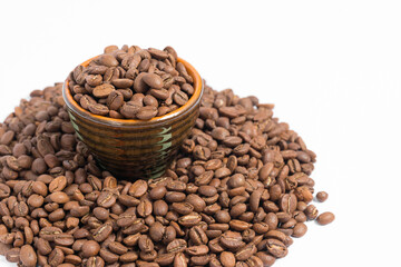 A small saucer with coffee beans stands on a pile of coffee on a white background.