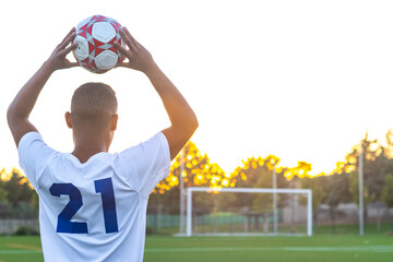 Football player raising the ball throw-in. Rear view of soccer player throwing the ball with his hands on the playing field. Football player doing throw-in