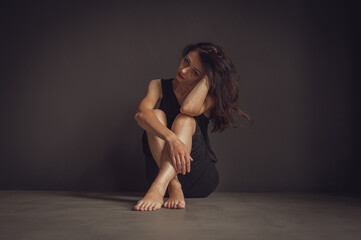 young pretty girl sitting on the floor, pensive, thinking, depression, dark background, low key