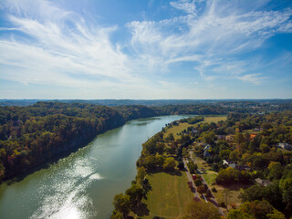 an aerial shot of a gorgeous autumn landscape along the silky green waters of the Tennessee River surrounded by autumn colored trees and lush green trees with blue sky and clouds at Sequoyah Park - obrazy, fototapety, plakaty