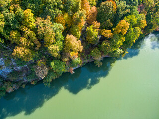an aerial shot of a gorgeous autumn landscape along the silky green waters of the Tennessee River surrounded by autumn colored trees and lush green trees with blue sky and clouds at Sequoyah Park - obrazy, fototapety, plakaty