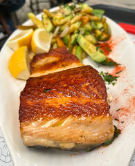Fried salmon fillet with french fries, lemon salad and vegetables served in black plate on wooden table