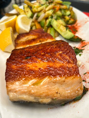 Fried salmon fillet with french fries, lemon salad and vegetables served in black plate on wooden table