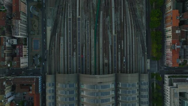 Birds eye shot of long passenger train leaving station and passing through switches in wide railway corridor.
