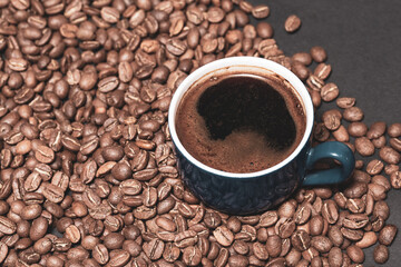 A cup of brewed black coffee on a dark background with beans.