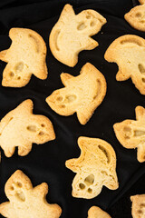 Baked butter cookies in ghost shapes formed by cookies cutter on black Halloween sweet treats - 538693935