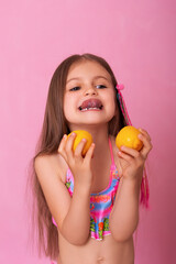 Caucasian beautiful little girl with fresh yellow lemons on a pink background.